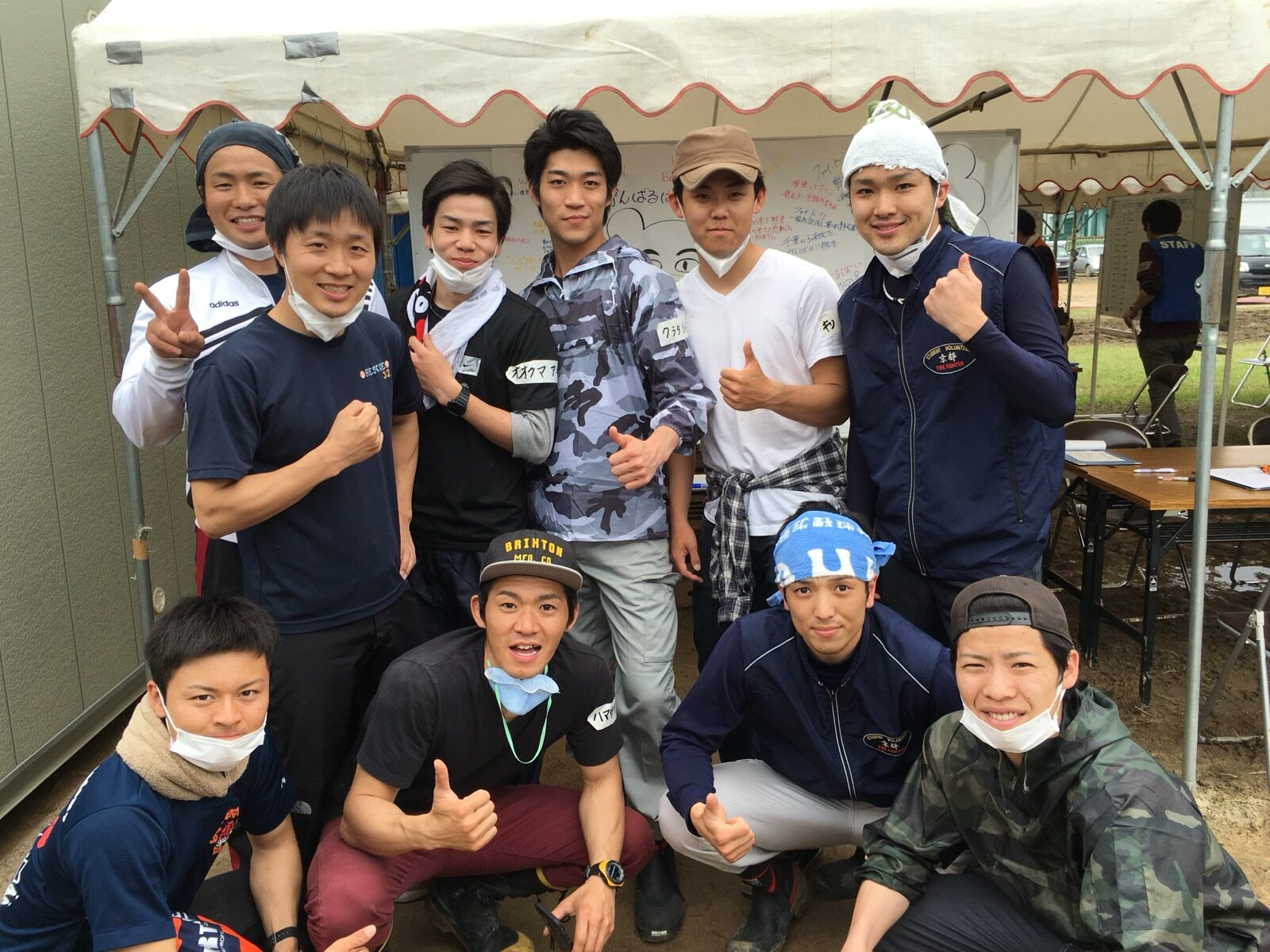 A group of young volunteers gathered under a relief tent giving thumbs-up after a day of disaster-relief work following the April 2016 Kumamoto earthquake