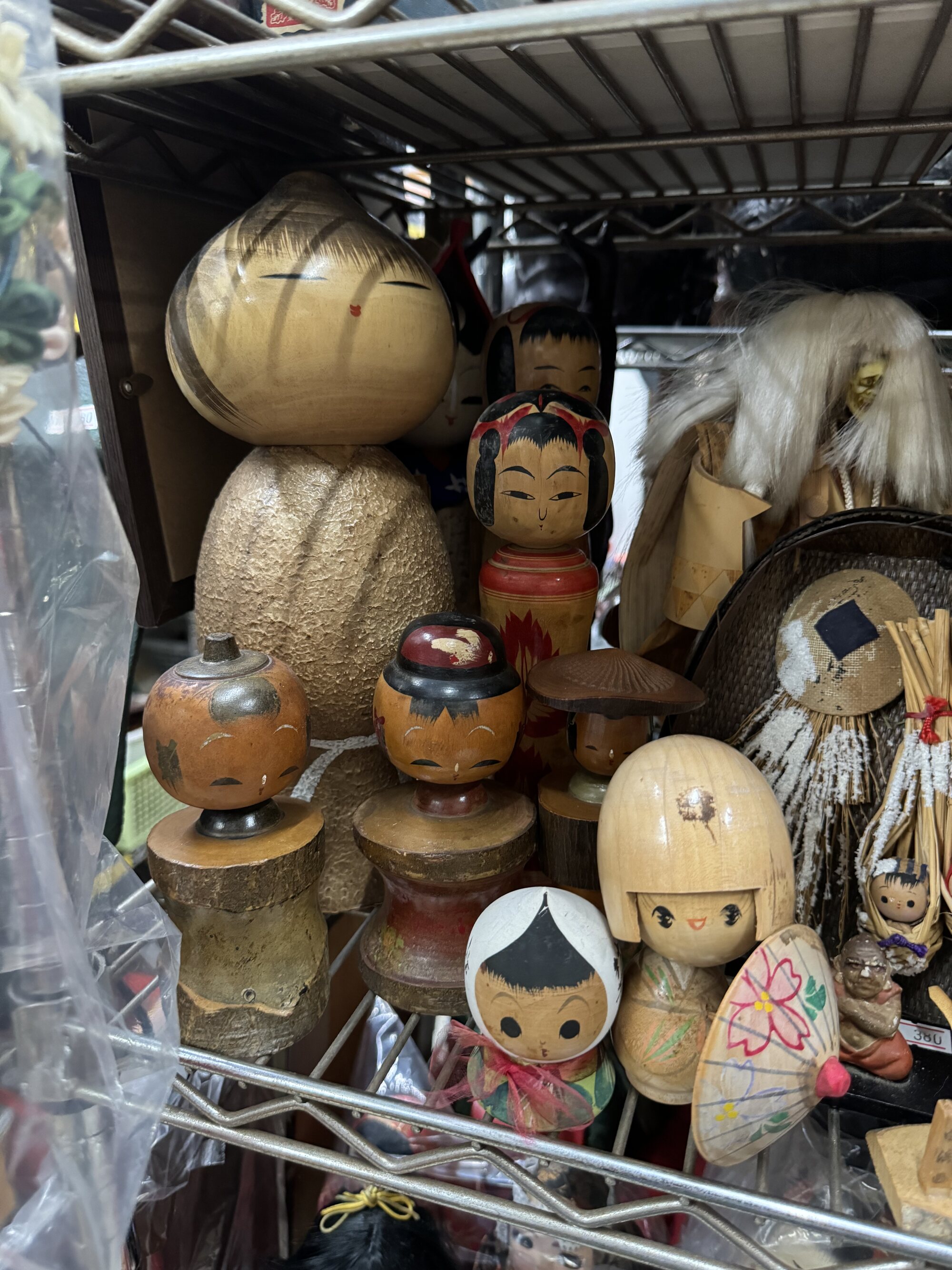Wooden kokeshi folk dolls and other carved crafts packed onto a wire-rack shelf and wrapped in plastic at a local Kyoto secondhand recycling shop.