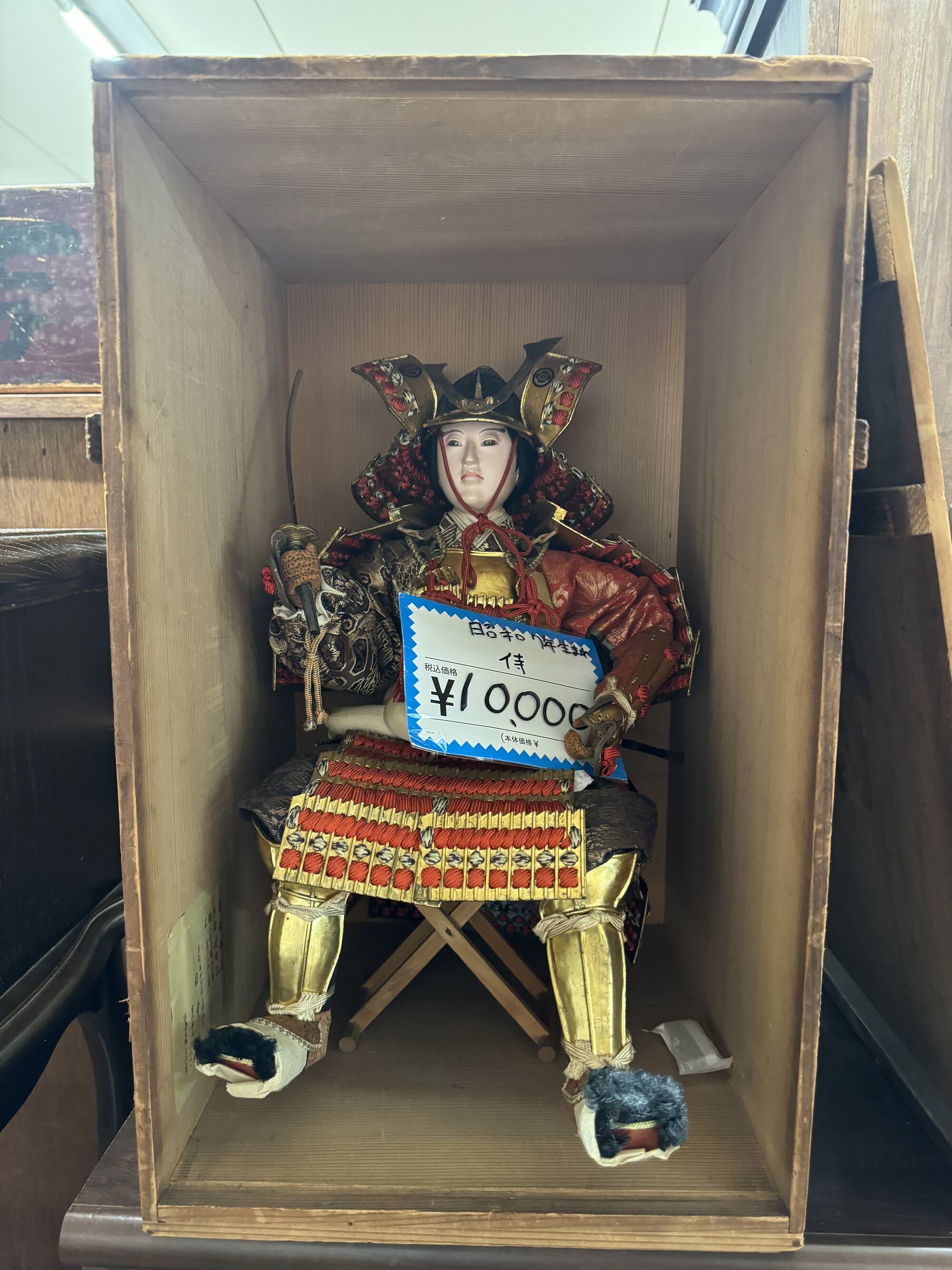 A boys-festival samurai armor doll (gogatsu ningyo) in a wooden display box with a 10,000 yen price tag, for sale at a local Kyoto secondhand recycling shop.