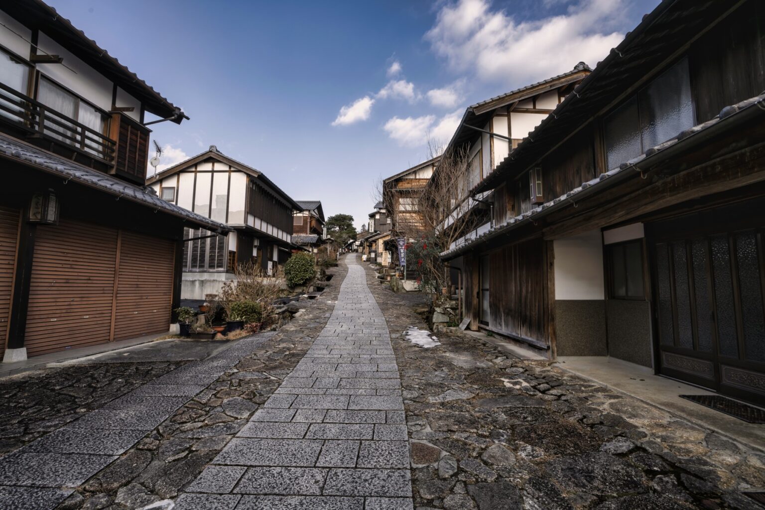 The granite-paved street of Magome-juku running between two-storey timber merchant houses under a blue winter sky with small patches of snow on the stones