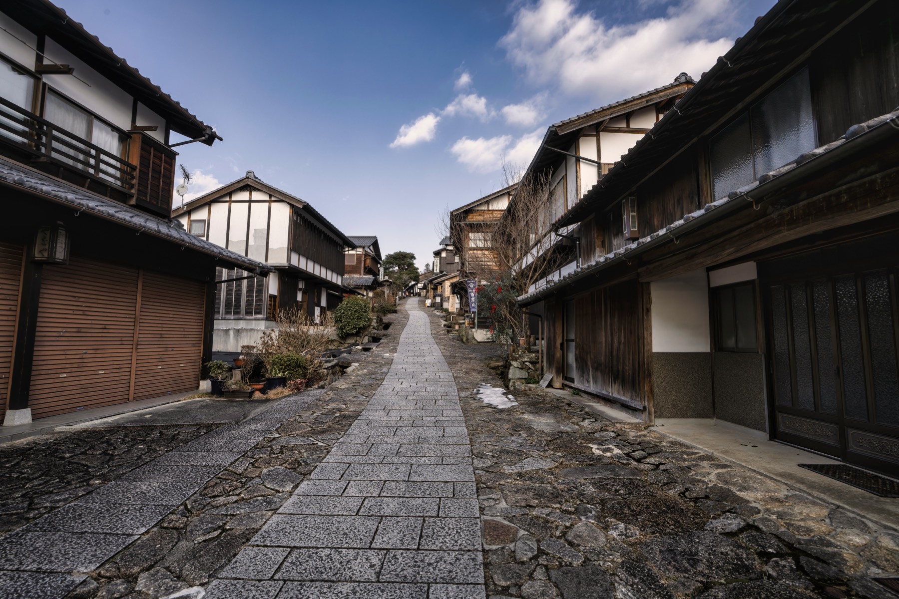 The granite-paved street of Magome-juku running between two-storey timber merchant houses under a blue winter sky with small patches of snow on the stones