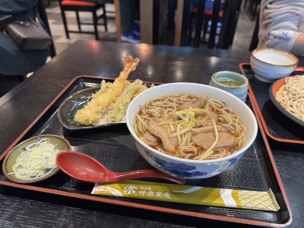 A duck seiro (kamo seiro) set at Minatoan Konandai in Yokohama: cold buckwheat soba, a bowl of hot duck-and-leek dipping broth, and a plate of shrimp and vegetable tempura on a black tray.