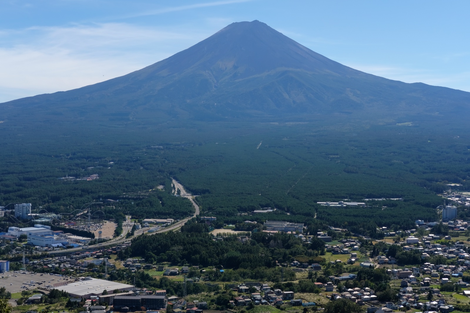 Mt Fuji rising above the Fuji Five Lakes basin, with the town and an amusement park spread across the forest below, seen from the Kawaguchiko panorama viewpoint