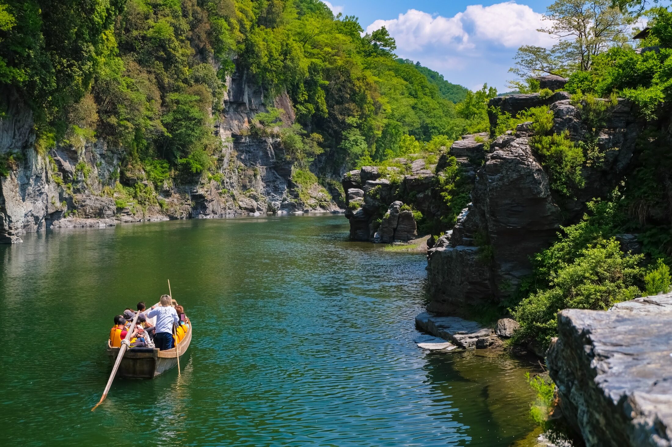 A traditional wooden boat carrying passengers down the emerald green Arakawa river between the rock terraces of Nagatoro gorge in summer