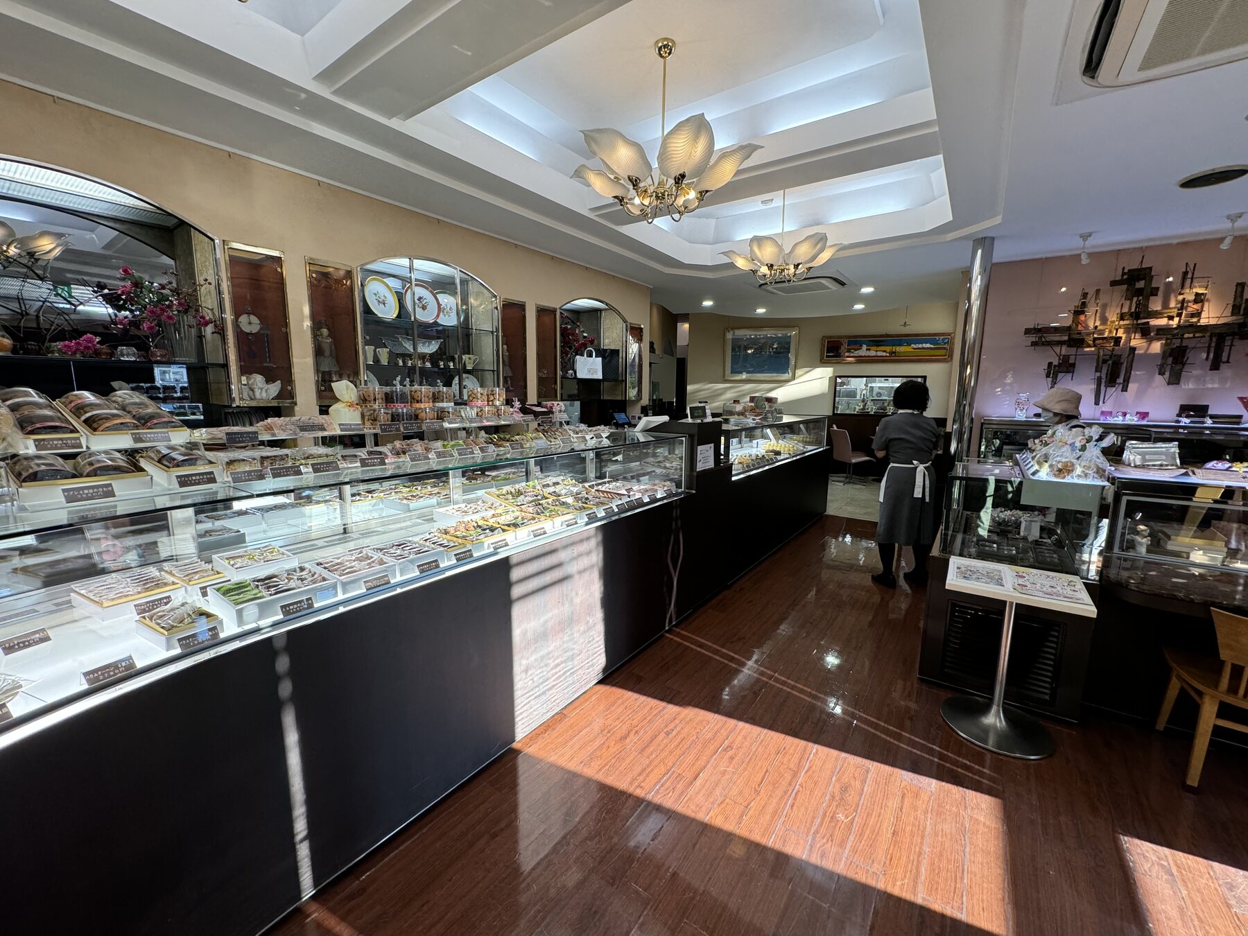 The elegant interior of Okashinoie Noe in Nerima, Tokyo, with a long glass patisserie case, polished wood floor and chandelier lighting in the shop's café and sales space.
