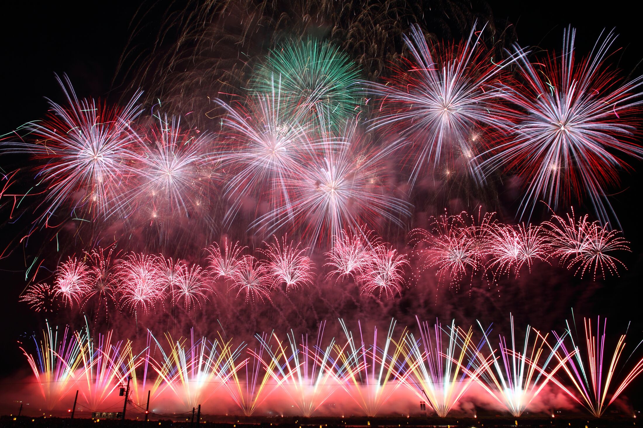 Layered red white and green competition fireworks filling the sky above the Omono River at the All-Japan National Fireworks Competition in Omagari, Akita
