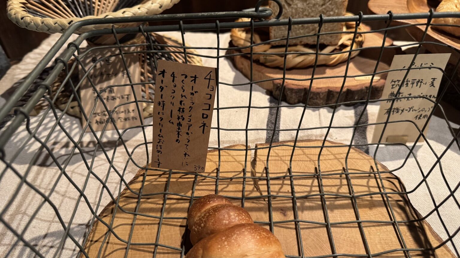 A loaf of Pandian's natural-yeast bread in a wire basket beside a small handwritten wooden price tag, in the wooden shop on Lake Kawaguchi in Fujikawaguchiko.
