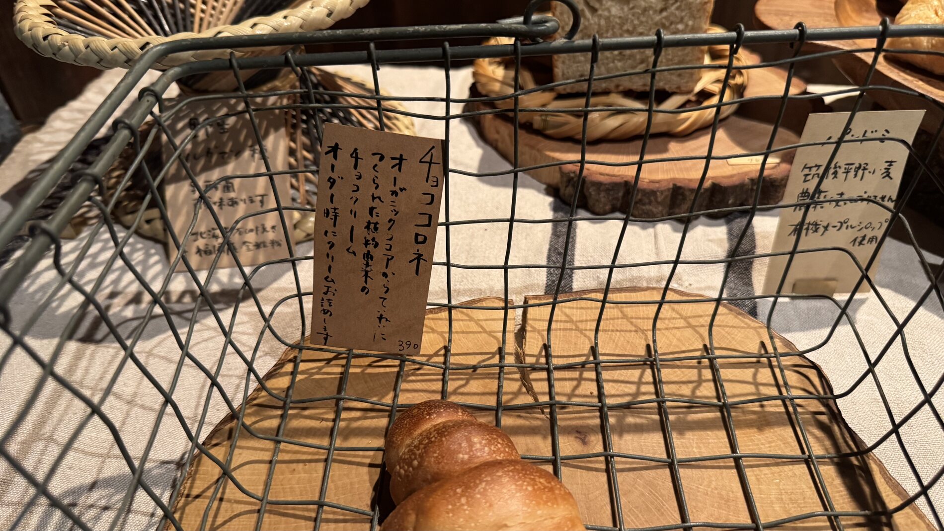 A loaf of Pandian's natural-yeast bread in a wire basket beside a small handwritten wooden price tag, in the wooden shop on Lake Kawaguchi in Fujikawaguchiko.