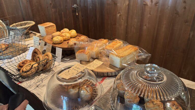 The bread display at Pandian bakery in Fujikawaguchiko: baskets and glass domes of natural-yeast loaves, buns and muffins with handwritten labels on a rustic counter.
