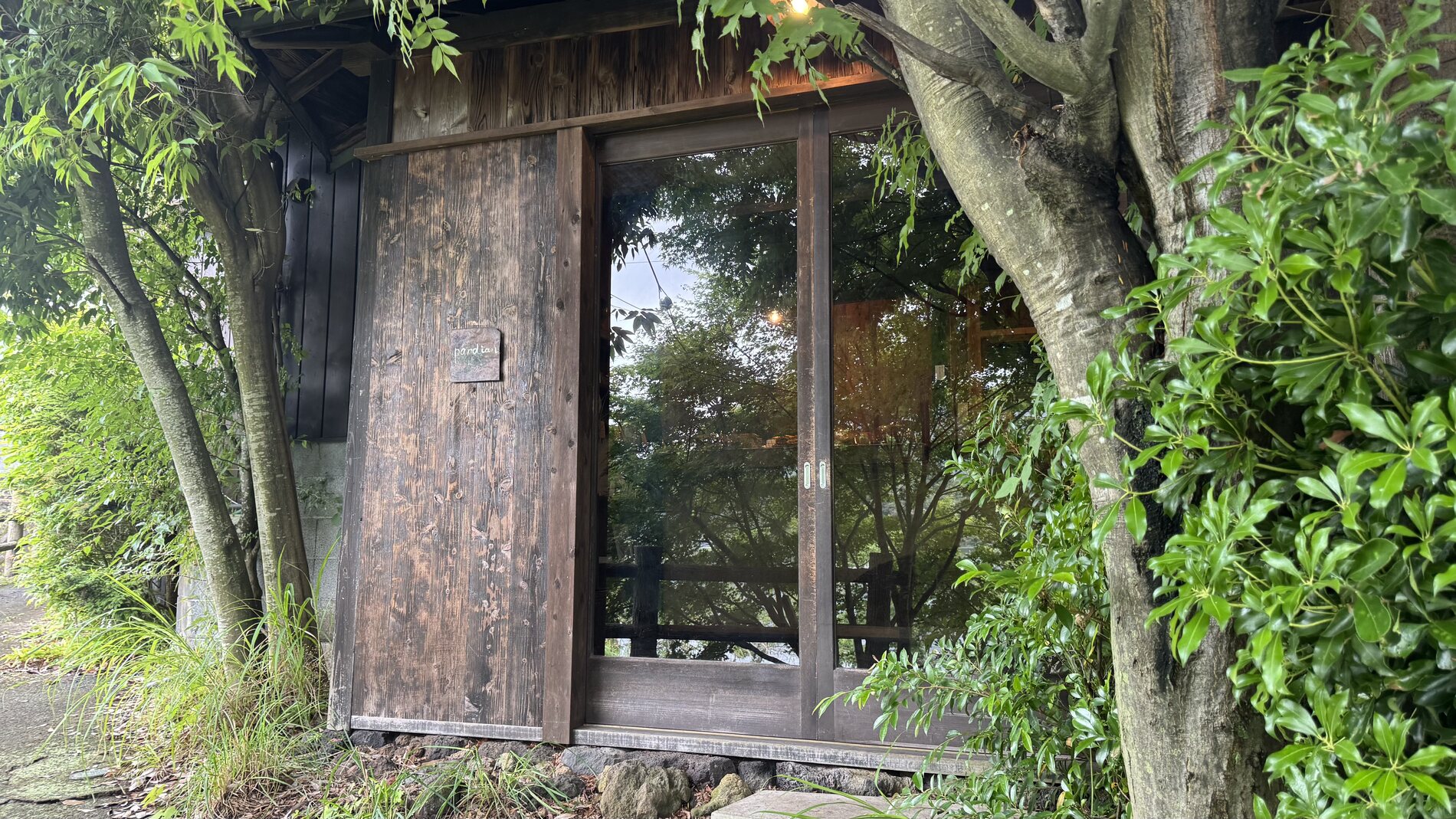 The weathered wooden entrance of Pandian bakery, framed by trees and a stone path, on the shore of Lake Kawaguchi in Fujikawaguchiko, Yamanashi.