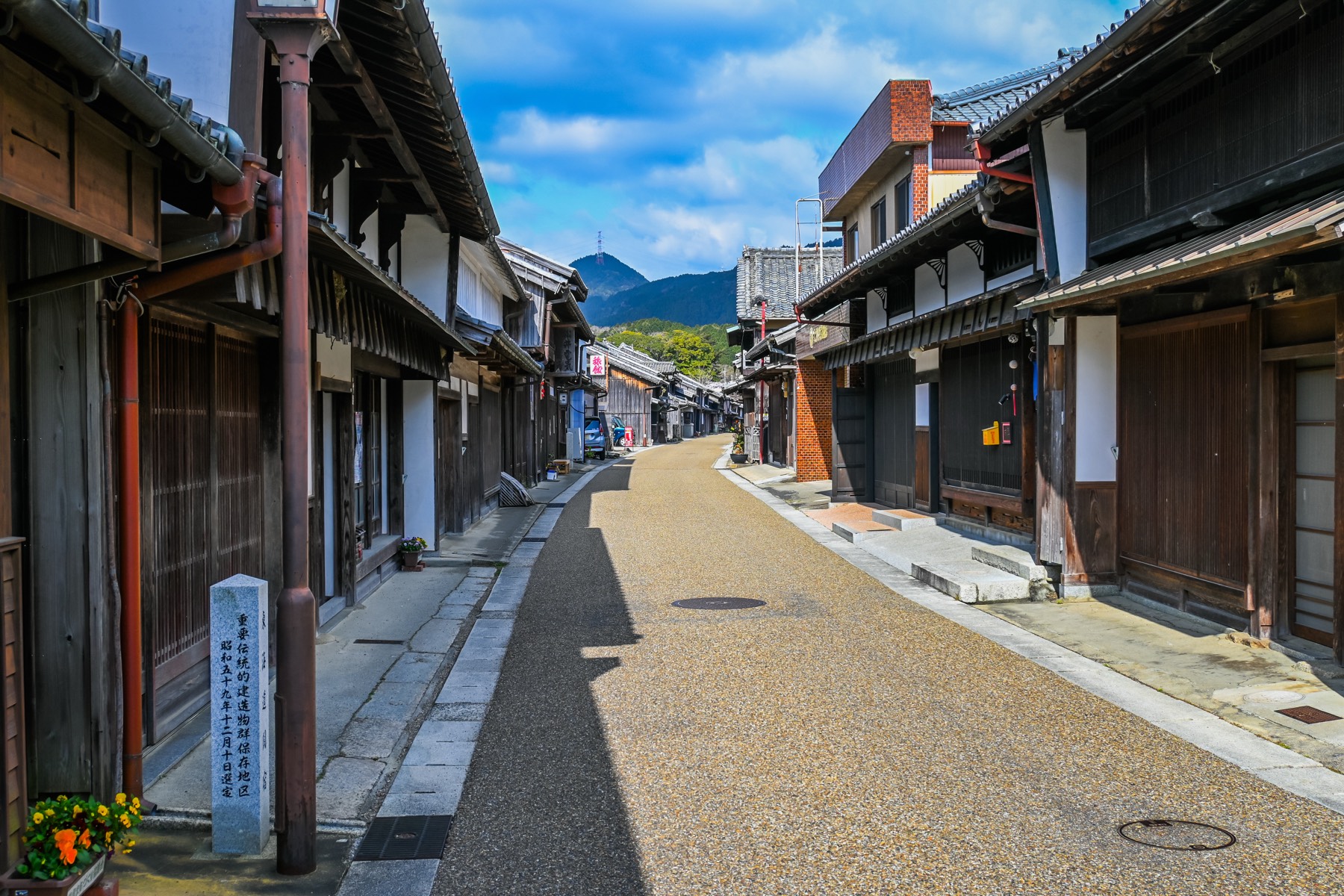 The Tokaido street of Seki-juku lined with traditional machiya on both sides a stone preservation-district marker in front and mountains at the far end