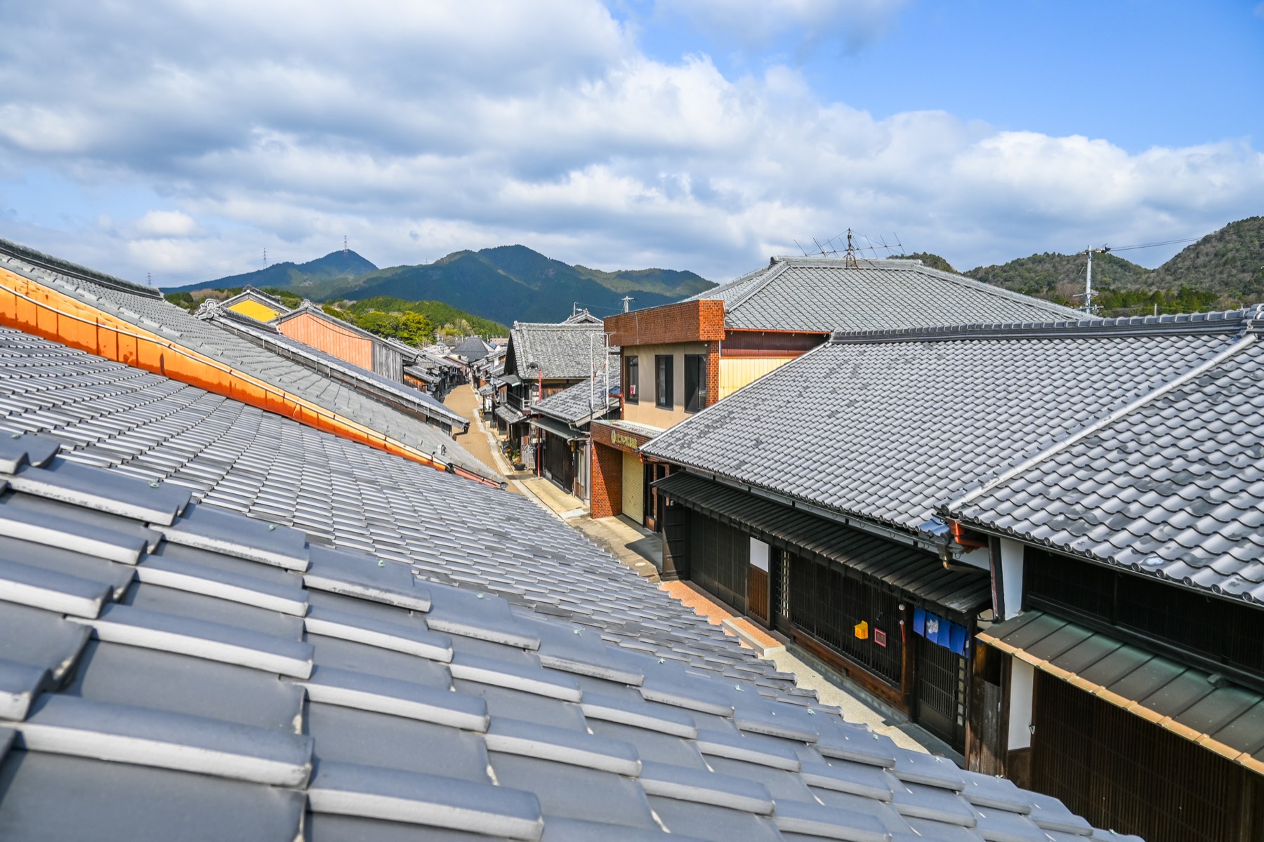 An elevated view over the grey tiled roofs of the Seki-juku townscape stretching toward green mountains under a blue sky