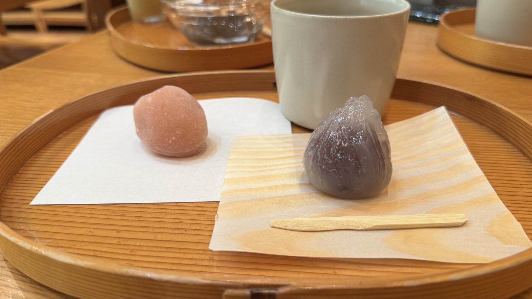 A pink ume mochi and a translucent kuzu manju served on a round wooden tray with a cup of sencha green tea at the Toraya Kobo cafe in Gotemba, Shizuoka