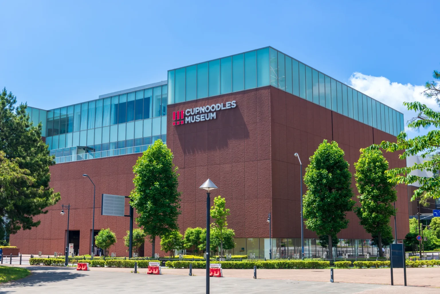 The red-brick cube exterior of the CupNoodles Museum in Yokohama Minatomirai under a clear blue sky, with the CUPNOODLES MUSEUM logo mounted on the corner of the facade
