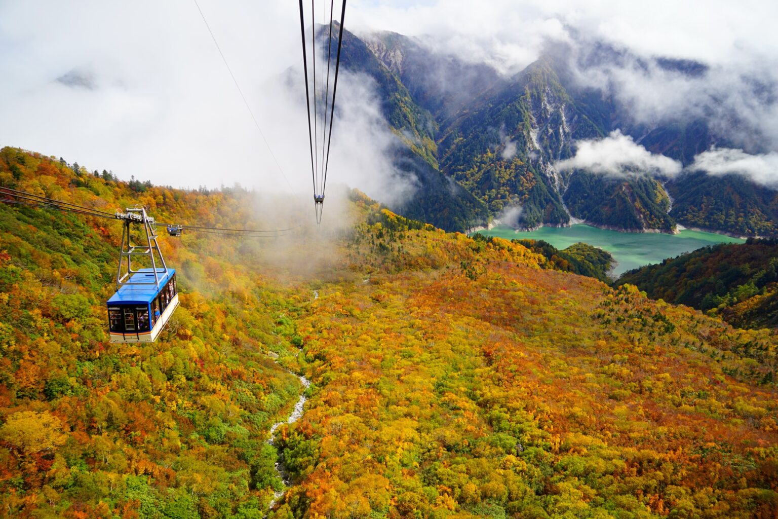The Tateyama Ropeway descending from Daikanbo station over slopes covered in red, orange and gold autumn colour on the Tateyama Kurobe Alpine Route, with the Kurobe valley far below