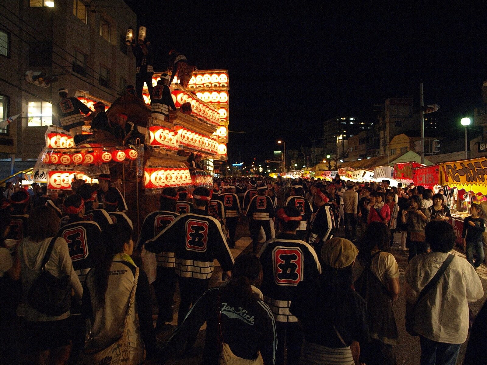 An ornately carved wooden danjiri float hung with glowing paper lanterns being pulled slowly through Kishiwada at night