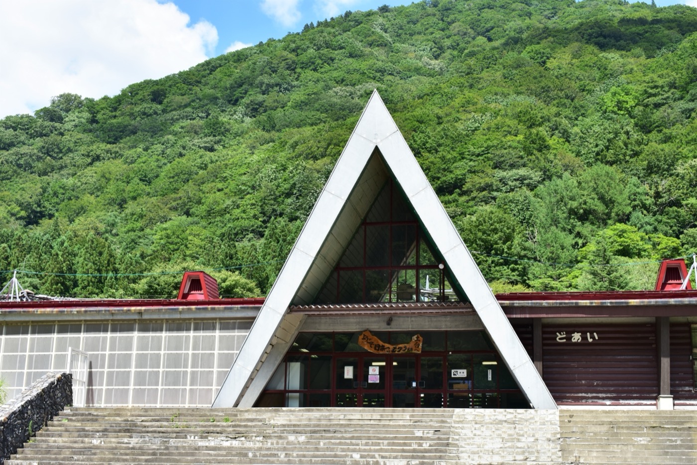 The triangular A-frame station building of Doai Station against green mountains, with a banner reading Japan's number-one mole station, Minakami, Gunma