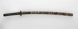 A Japanese katana sword in an ornate black-and-gold lacquered mounting, the kind of blade made from tatara-smelted tamahagane steel