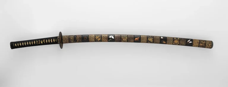 A Japanese katana sword in an ornate black-and-gold lacquered mounting, the kind of blade made from tatara-smelted tamahagane steel