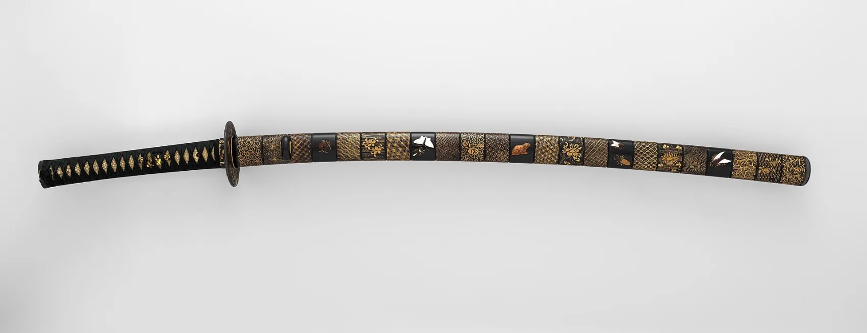 A Japanese katana sword in an ornate black-and-gold lacquered mounting, the kind of blade made from tatara-smelted tamahagane steel