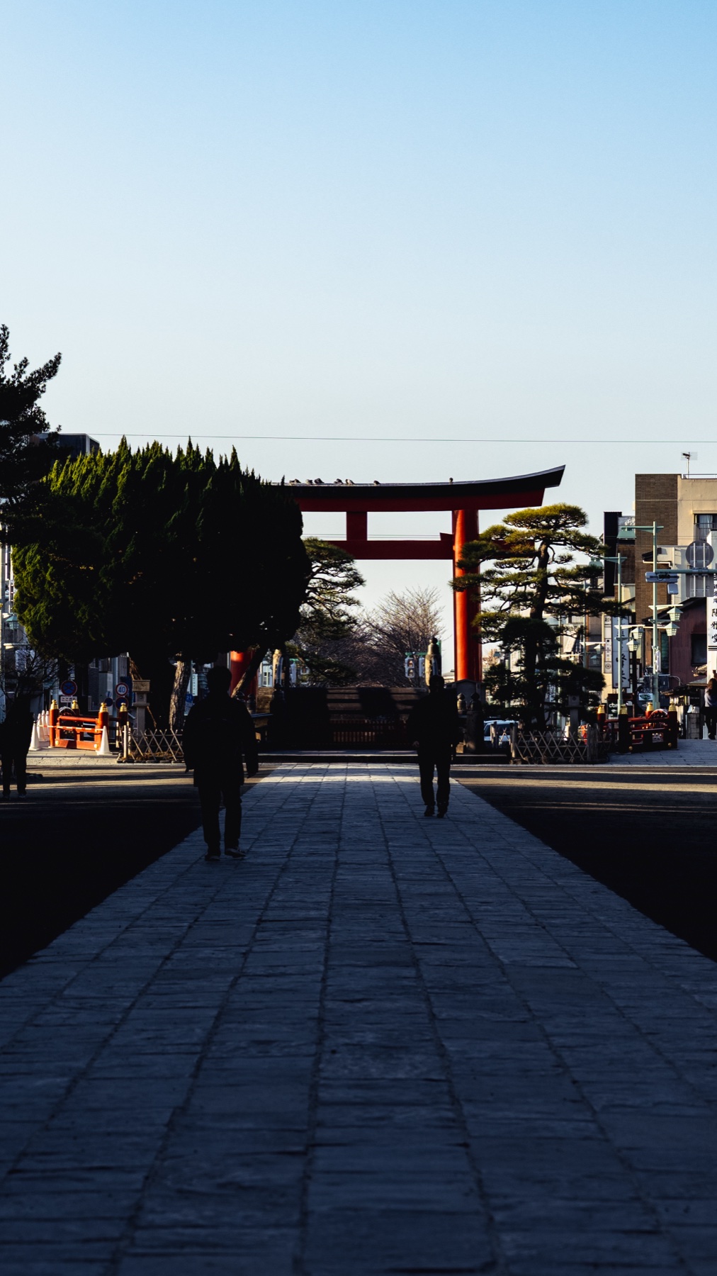 Early morning on the raised Dankazura walkway on Wakamiya Oji street in Kamakura, looking toward the red second torii gate of Tsurugaoka Hachimangu with only two people walking the stone path