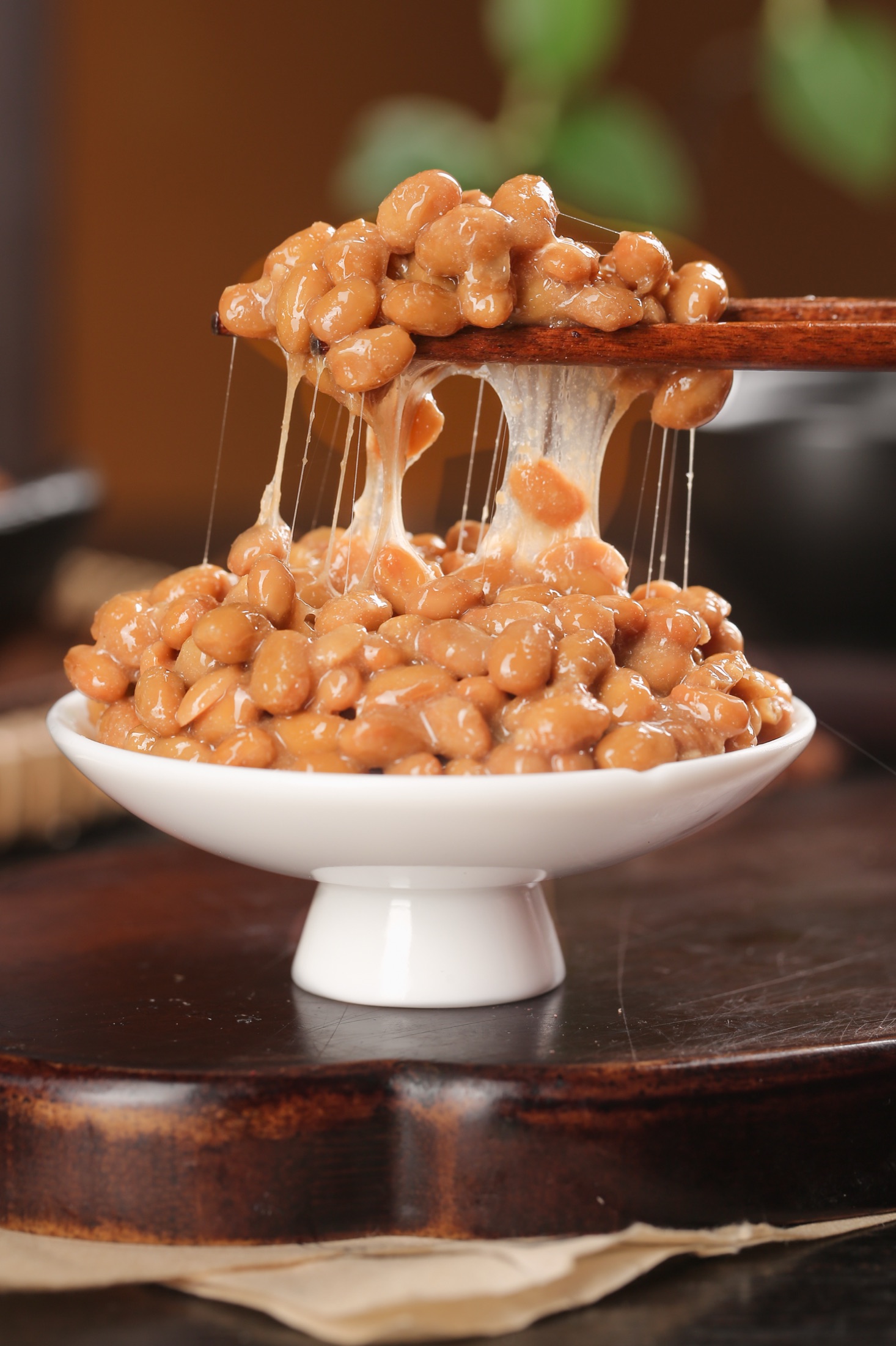 Chopsticks lifting fermented natto soybeans from a white bowl, stretching the long glossy sticky threads known as neba-neba that define the texture of Japan traditional fermented soybean breakfast food