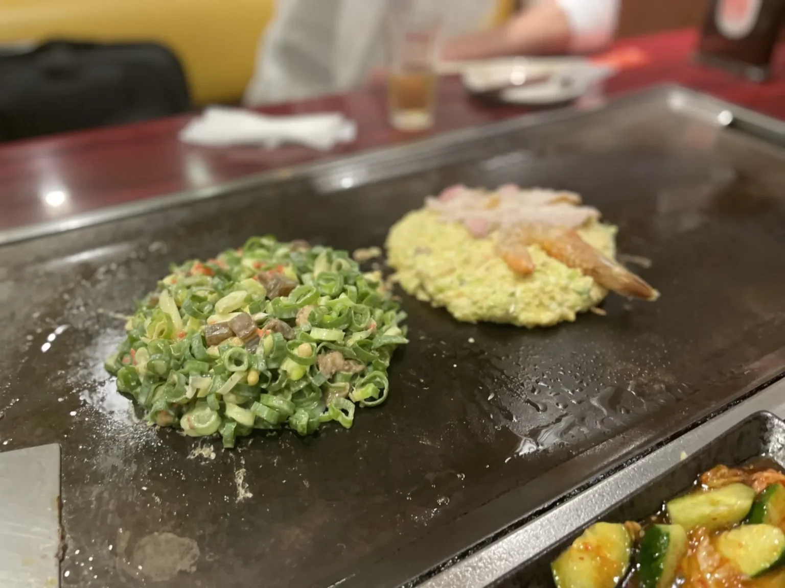 Two okonomiyaki cooking on a steel teppan grill in an Osaka restaurant