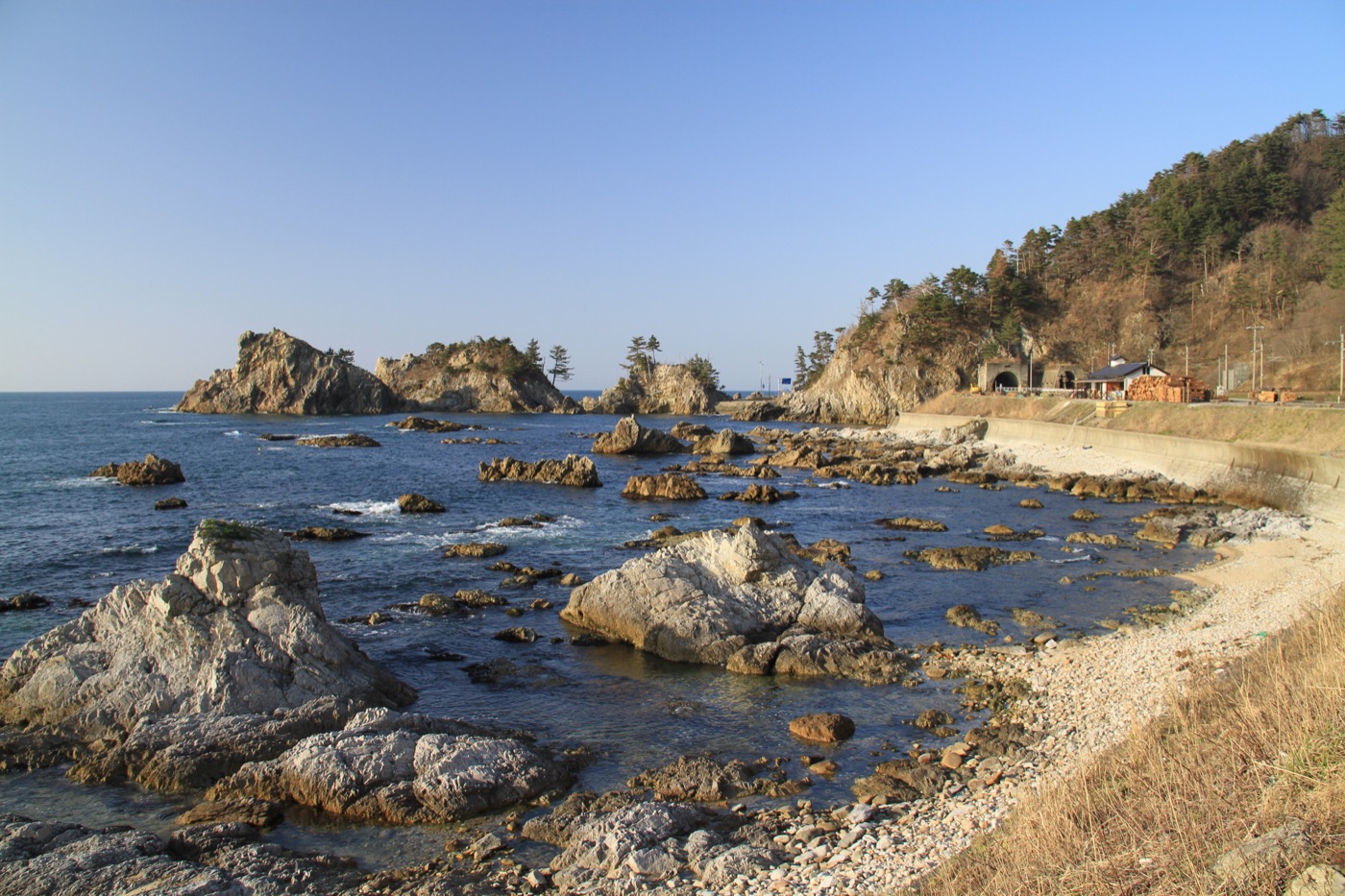 The clear water and eroded rock formations of the Sasagawa Nagare coastline with the coastal road and tunnel near Murakami, Niigata