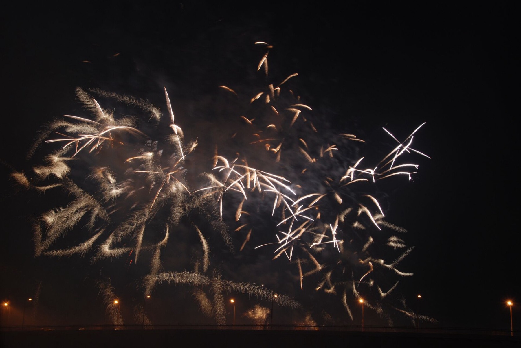 Golden willow fireworks cascading low over the Yodogawa river with a bridge silhouette in Osaka