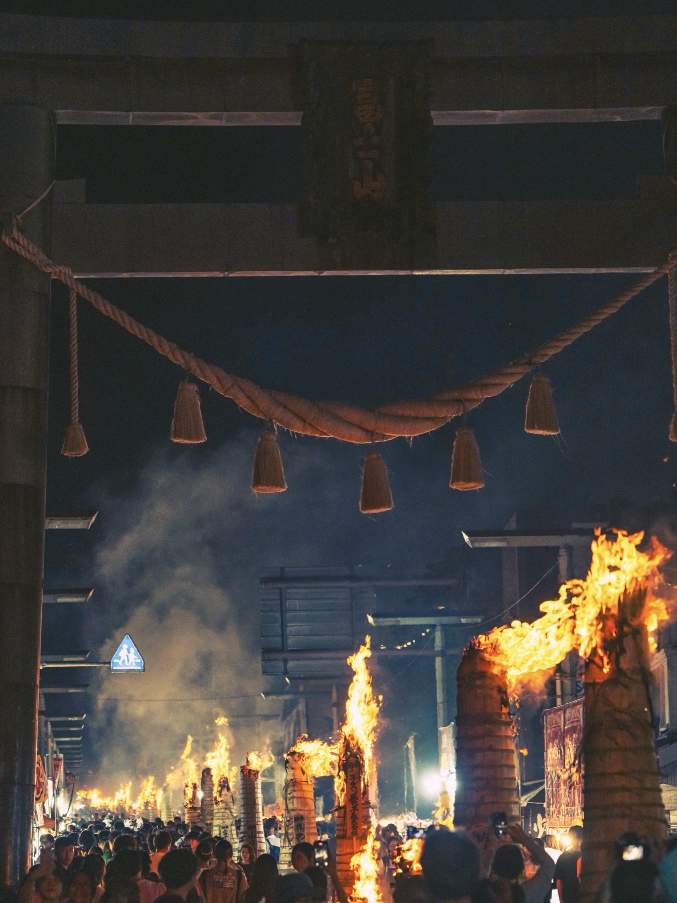 Smoke drifts through the great Kanadorii gate as dozens of taimatsu torch fires stretch down the main street of Fujiyoshida into the distance during the Yoshida Fire Festival evening.