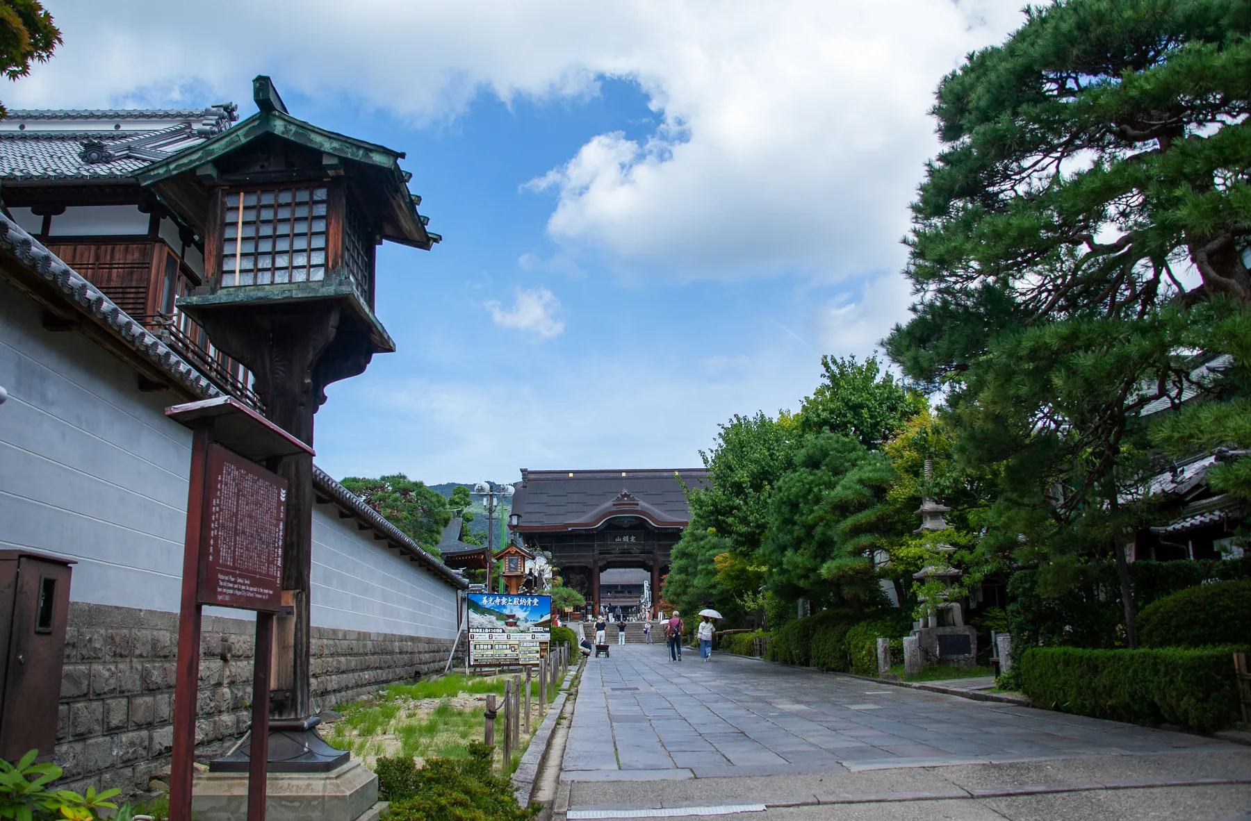 The stone-paved omotesando approach street to Zenkoji temple lined with stone lanterns and traditional shopfronts under a clear sky in Nagano City