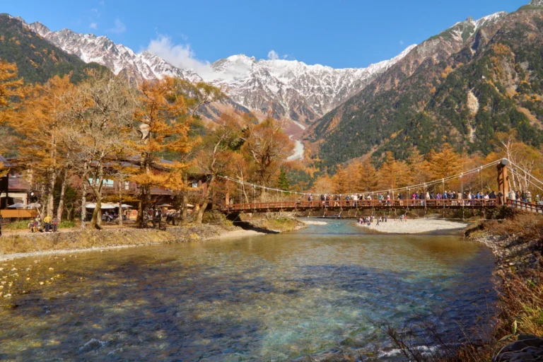 Kappa-bashi suspension bridge at Kamikochi with golden larch trees and snow-dusted Hotaka peaks