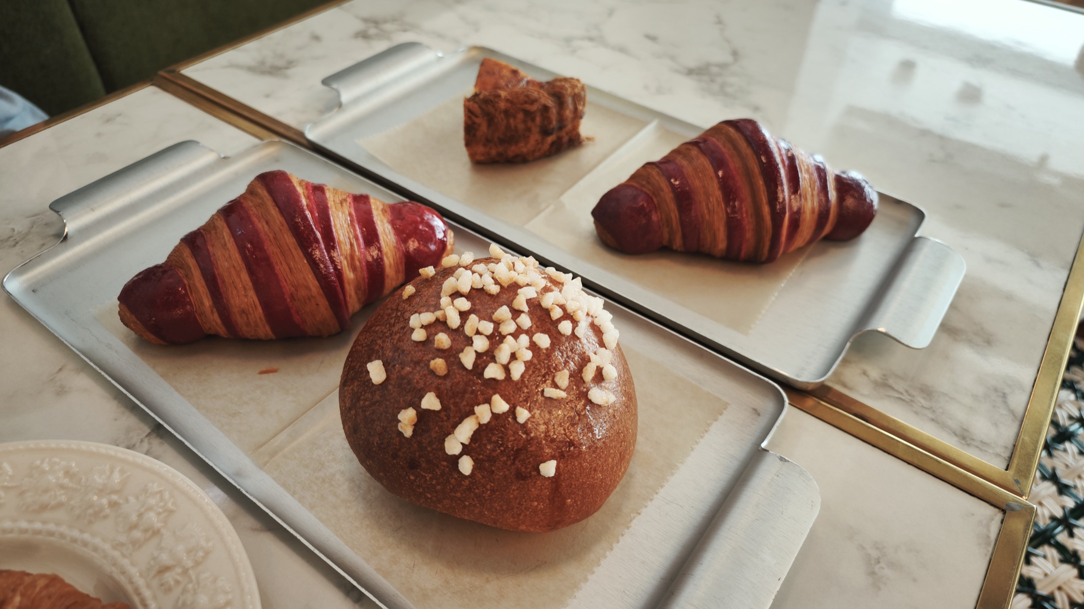 A tray at Liberte Kichijoji holding two croissants with deep burgundy stripes across the laminated pastry, a domed roll topped with irregular white grains and a small dark layered pastry