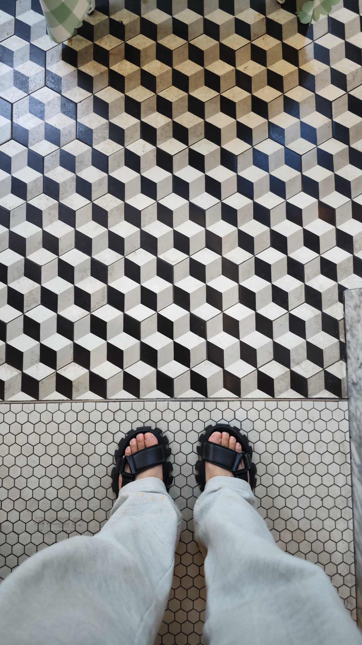 The floor at Liberte Kichijoji where a black, white and cream tumbling-block tile pattern meets plain white hexagonal tiling, photographed looking down