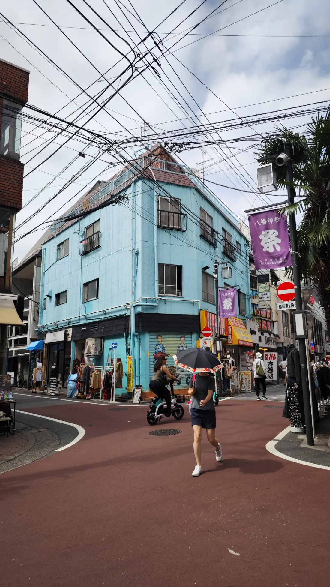 A mint-green tiled corner building on a red-paved Shimokitazawa street, with pedestrians crossing, a red no-entry sign and a tangle of overhead power lines overhead.