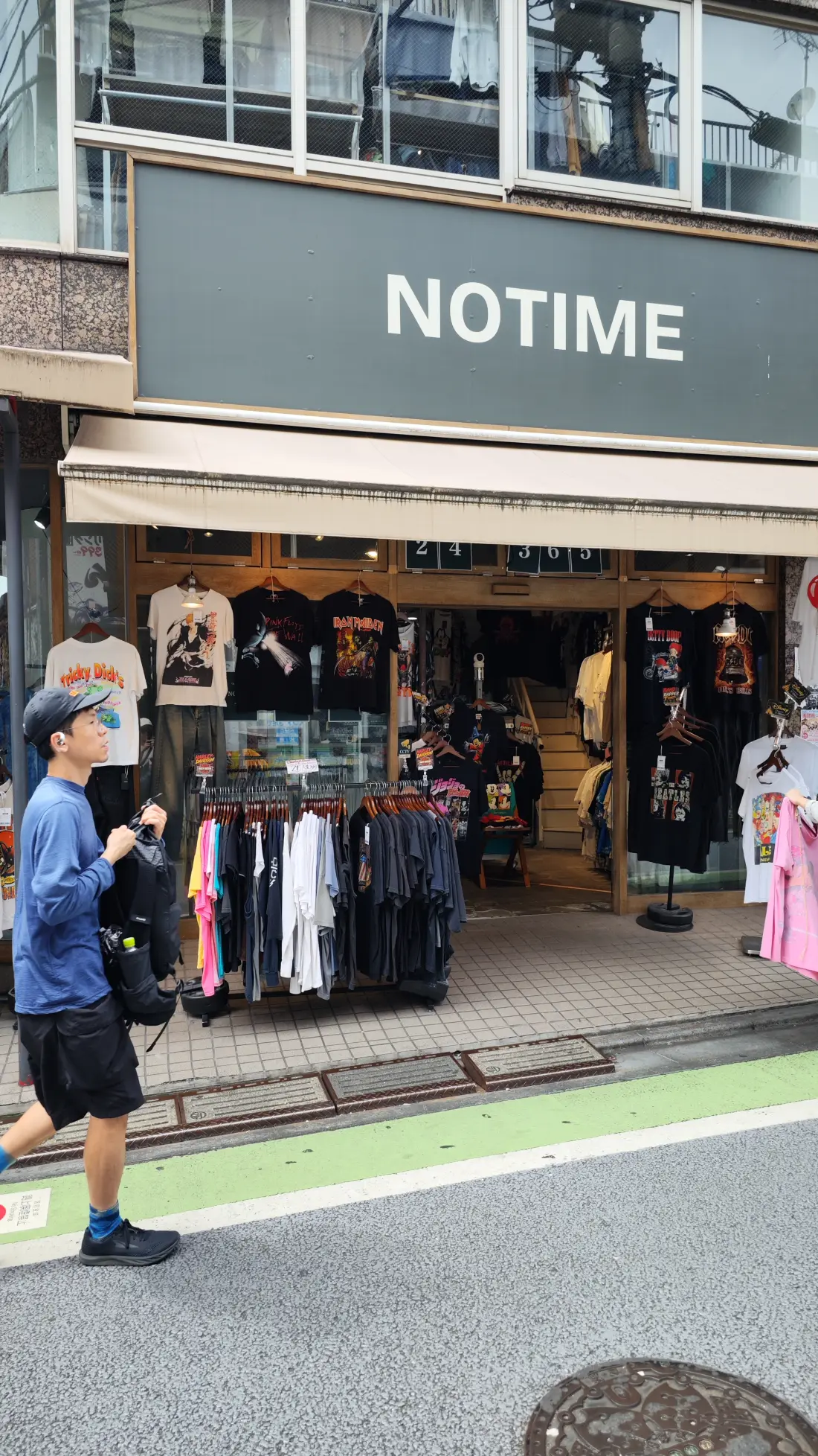 The storefront of a Shimokitazawa vintage-clothing shop with a sign reading NOTIME, racks of clothes spilling onto the pavement and a pedestrian walking past it.
