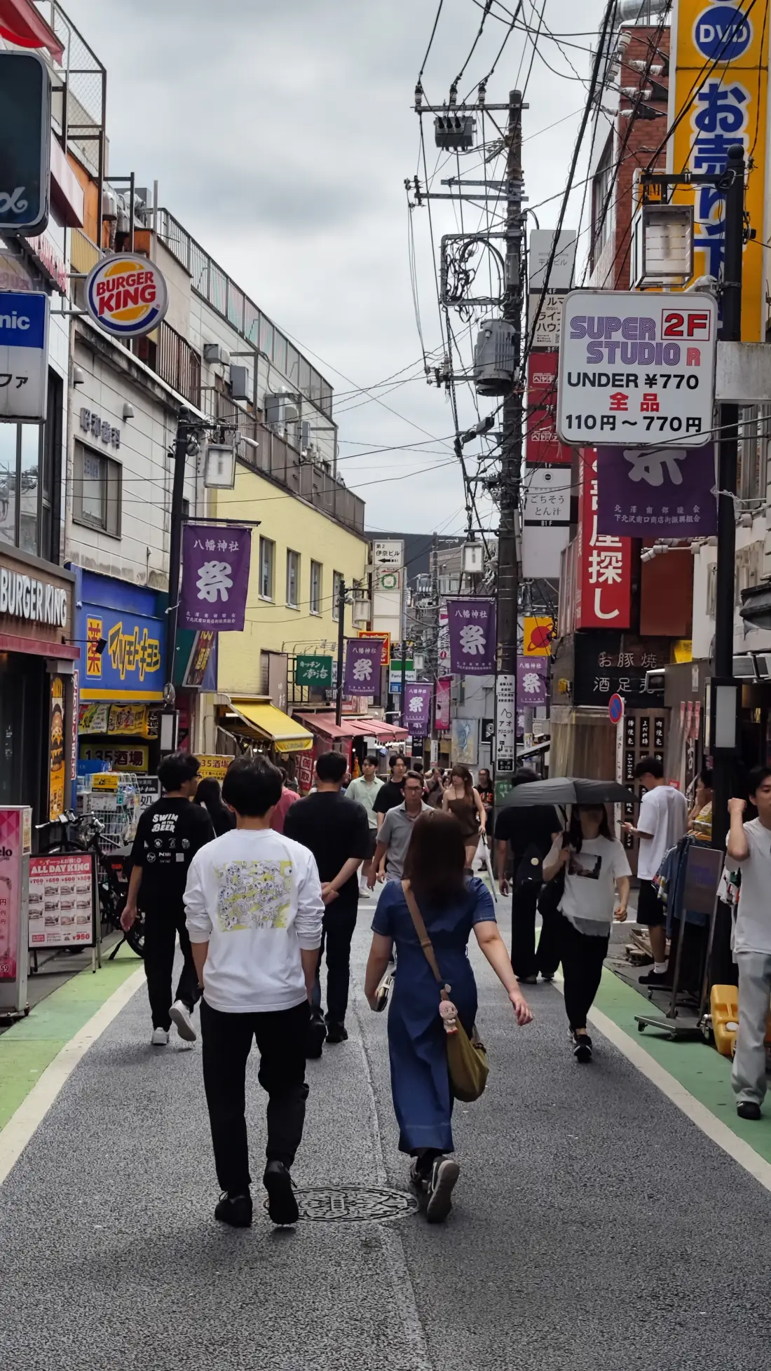 A hanging shop sign in Shimokitazawa reading SUPER STUDIO 2F, Under 770 yen, with all items priced from 110 to 770 yen, surrounded by cables and purple festival banners.