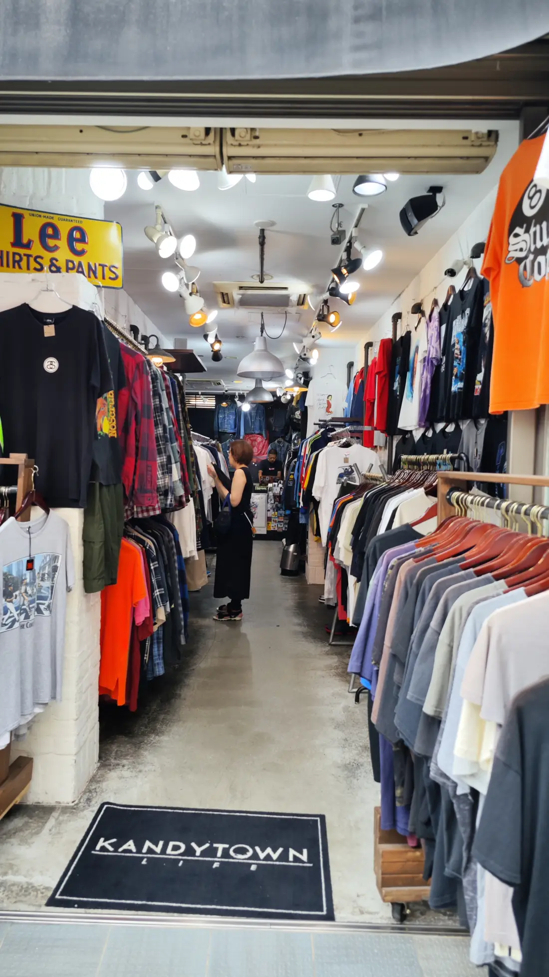 The inside of a Shimokitazawa second-hand clothing shop, with rails of shirts and jackets packed along both walls and a Lee shirts and pants sign near the ceiling.