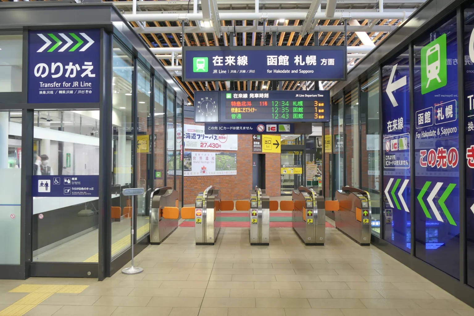 Ticket gates at Shin-Hakodate-Hokuto Station marked Transfer for JR Line, with an overhead sign for JR Line trains to Hakodate and Sapporo and a departure board above the gates.