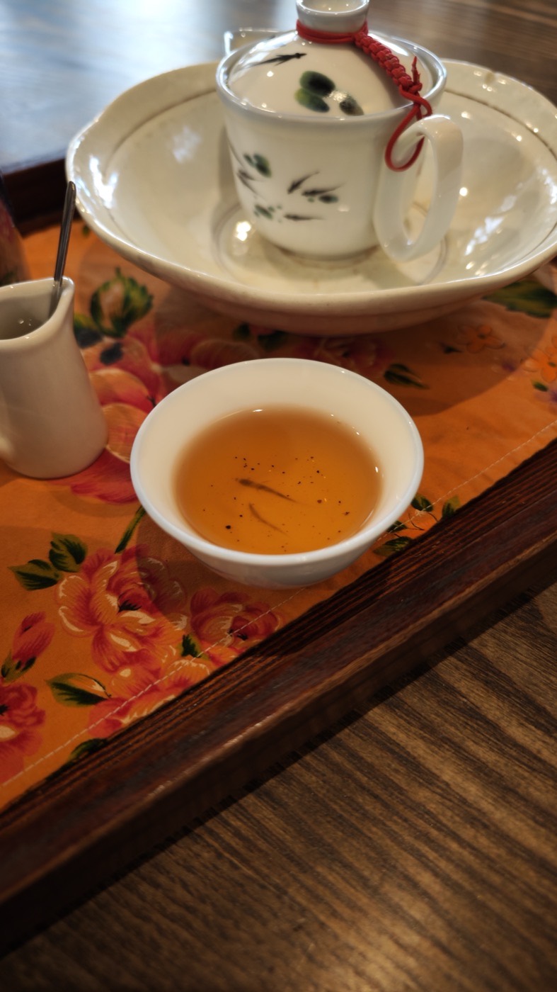 Small white cup of amber Taiwanese tea with leaf fragments, on an orange floral cloth