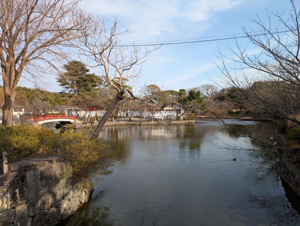 The vermilion main shrine of Tsurugaoka Hachimangu seen from the great stone stairway plaza, with the dance pavilion roof in the foreground, Kamakura
