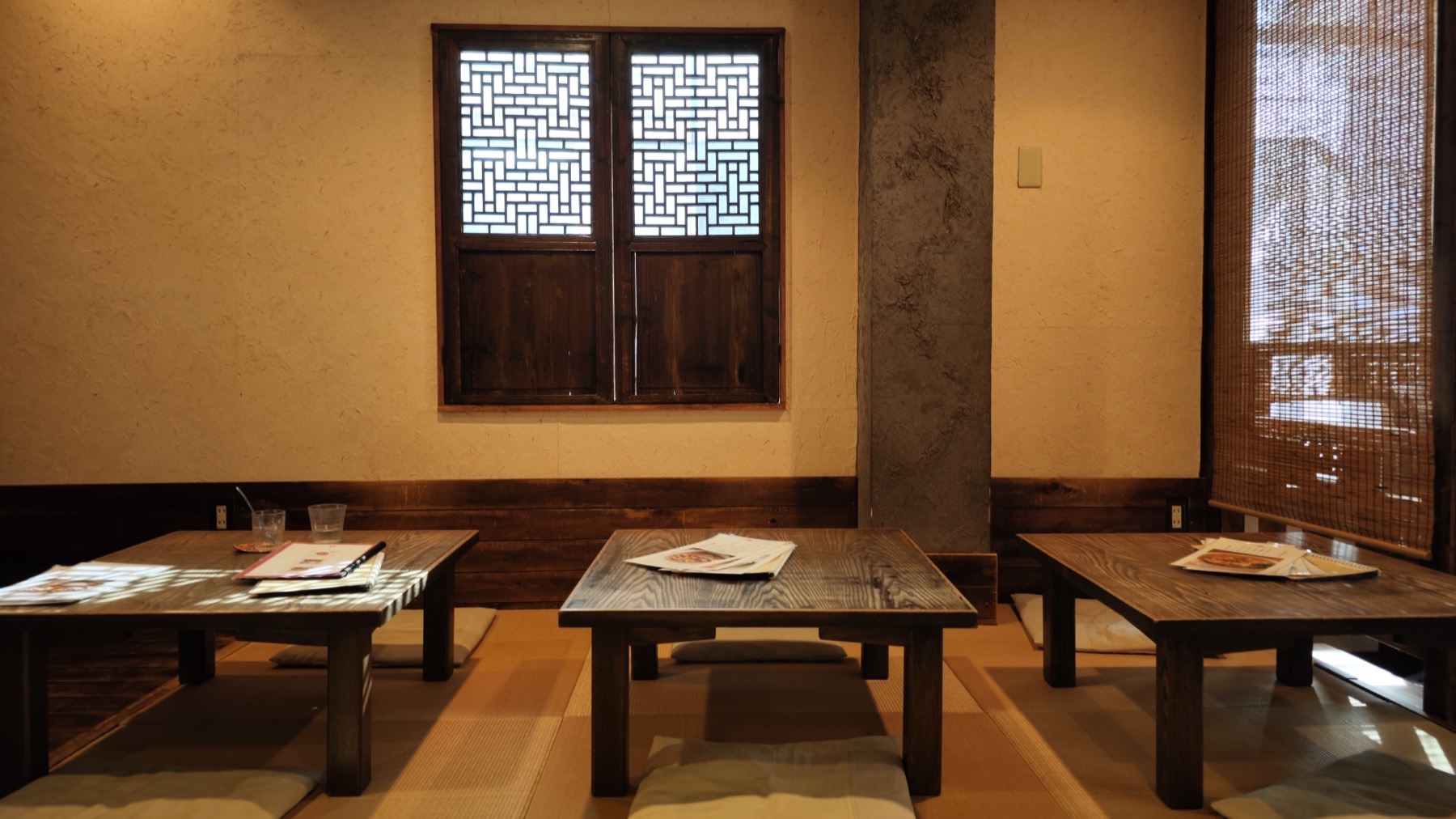 Tatami room at Yue He Cha Kichijoji with low wooden tables, floor cushions, a carved lattice window and bamboo blinds