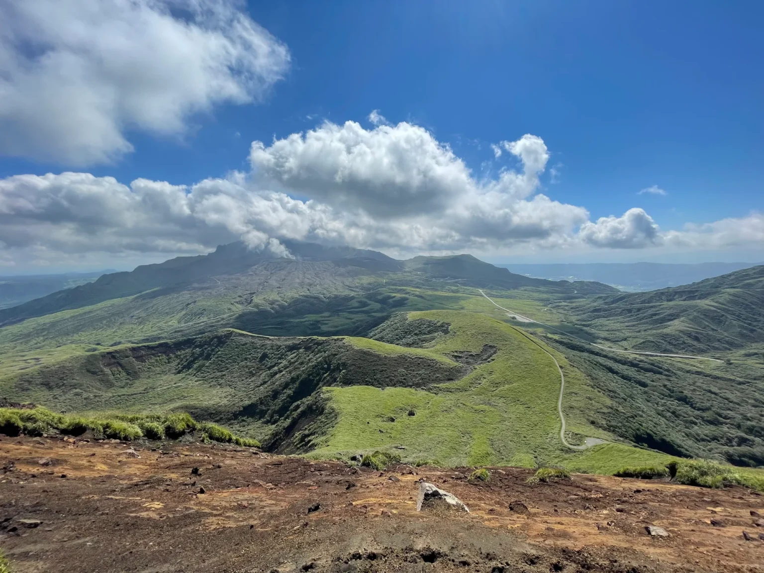 A white plume rising from Nakadake beyond green ridges, seen from Kishimadake.