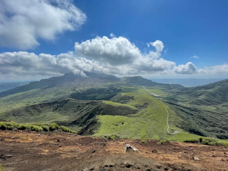 A white plume rising from Nakadake beyond green ridges, seen from Kishimadake.