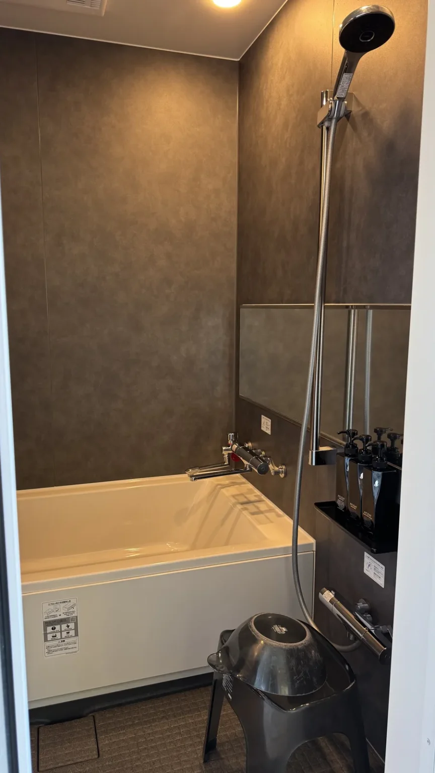 An indoor bathroom with a white bathtub, a wall-mounted shower and a bath stool and bowl