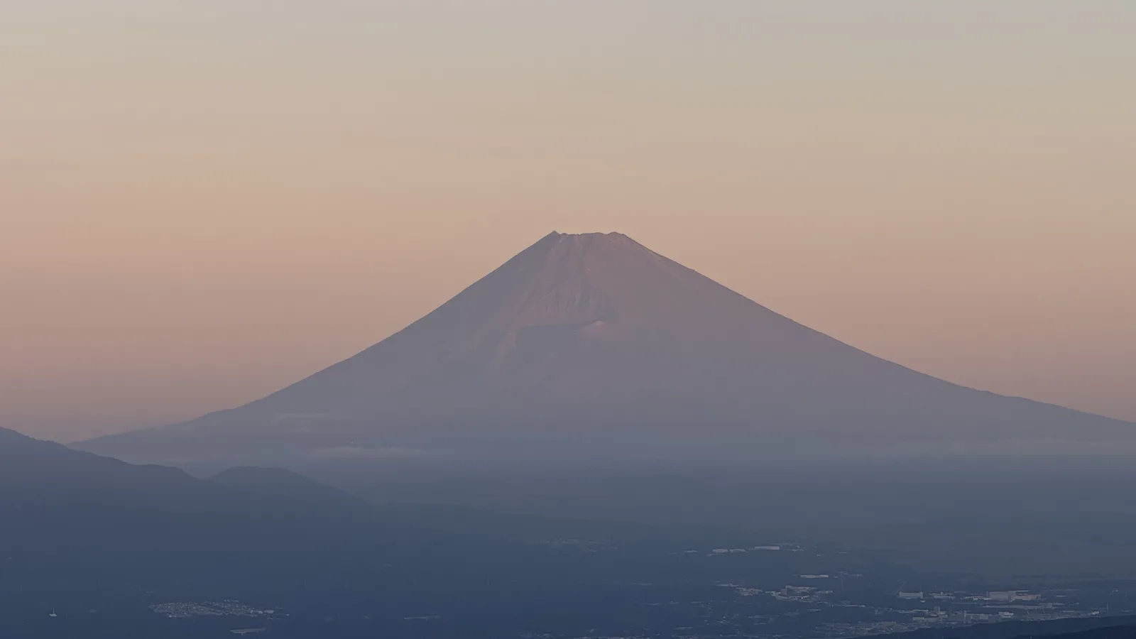 Mt Fuji in soft pink morning light above a hazy plain, seen from the Izu Skyline