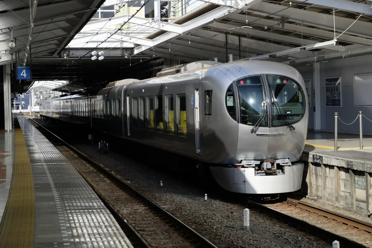 A silver Seibu Laview train with a rounded front standing at platform 4 under a station roof