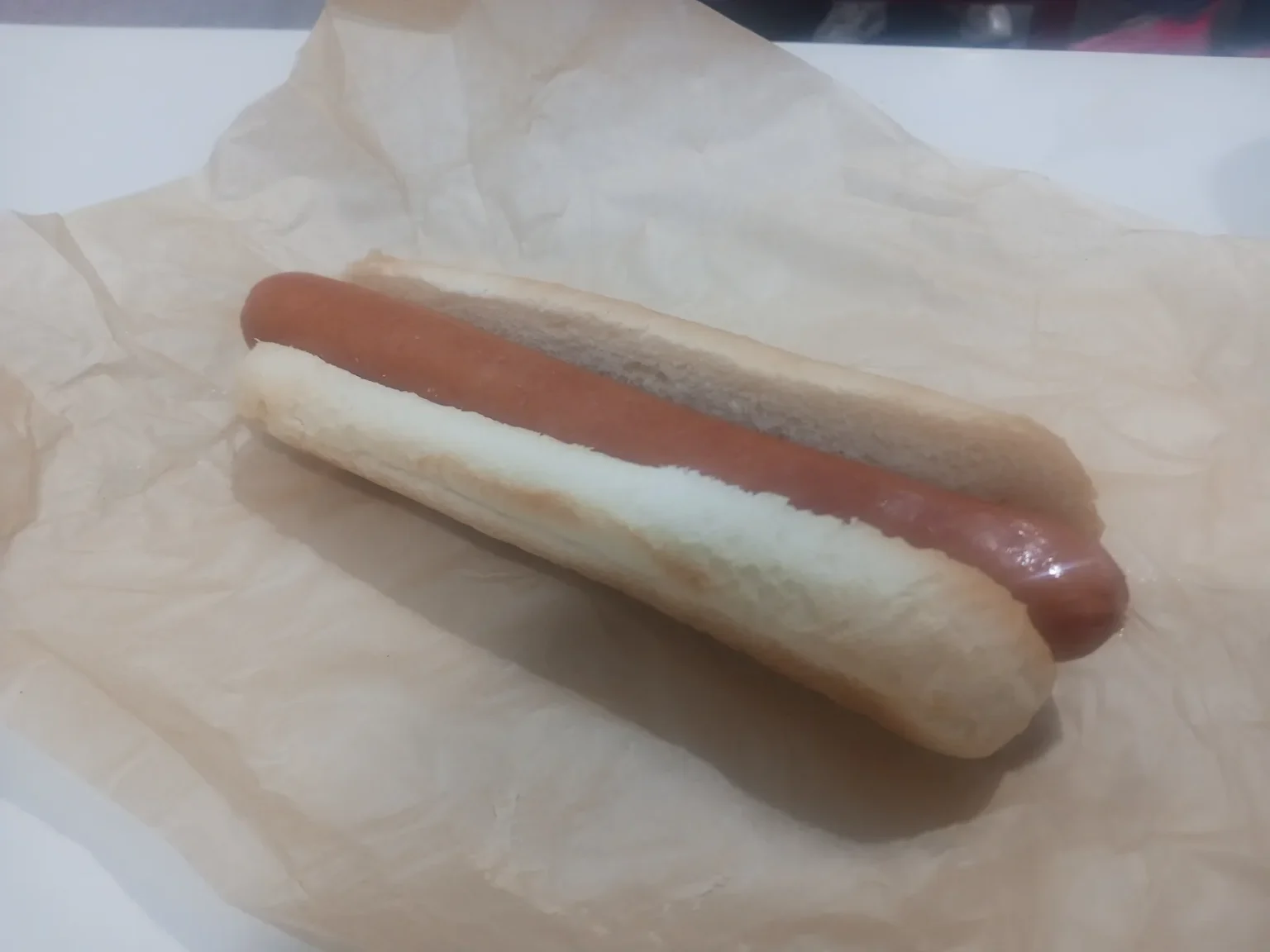 A plain hot dog in a white bun on crumpled brown paper on a white table