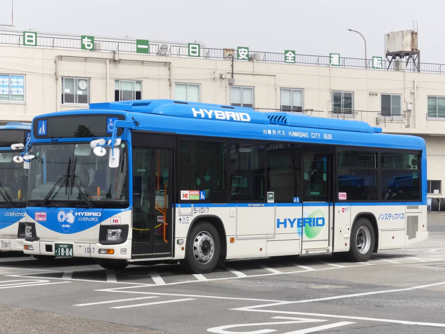 A blue and white Kawasaki City Bus hybrid single-decker parked at a depot, with the words Kawasaki City Bus along its side