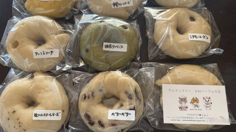 Bagged rice-flour bagels with handwritten Japanese flavour labels and a shop card reading グルテンフリー 米粉ベーグルの店
